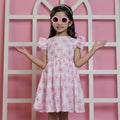Young girl in a pink floral dress standing against a pink background